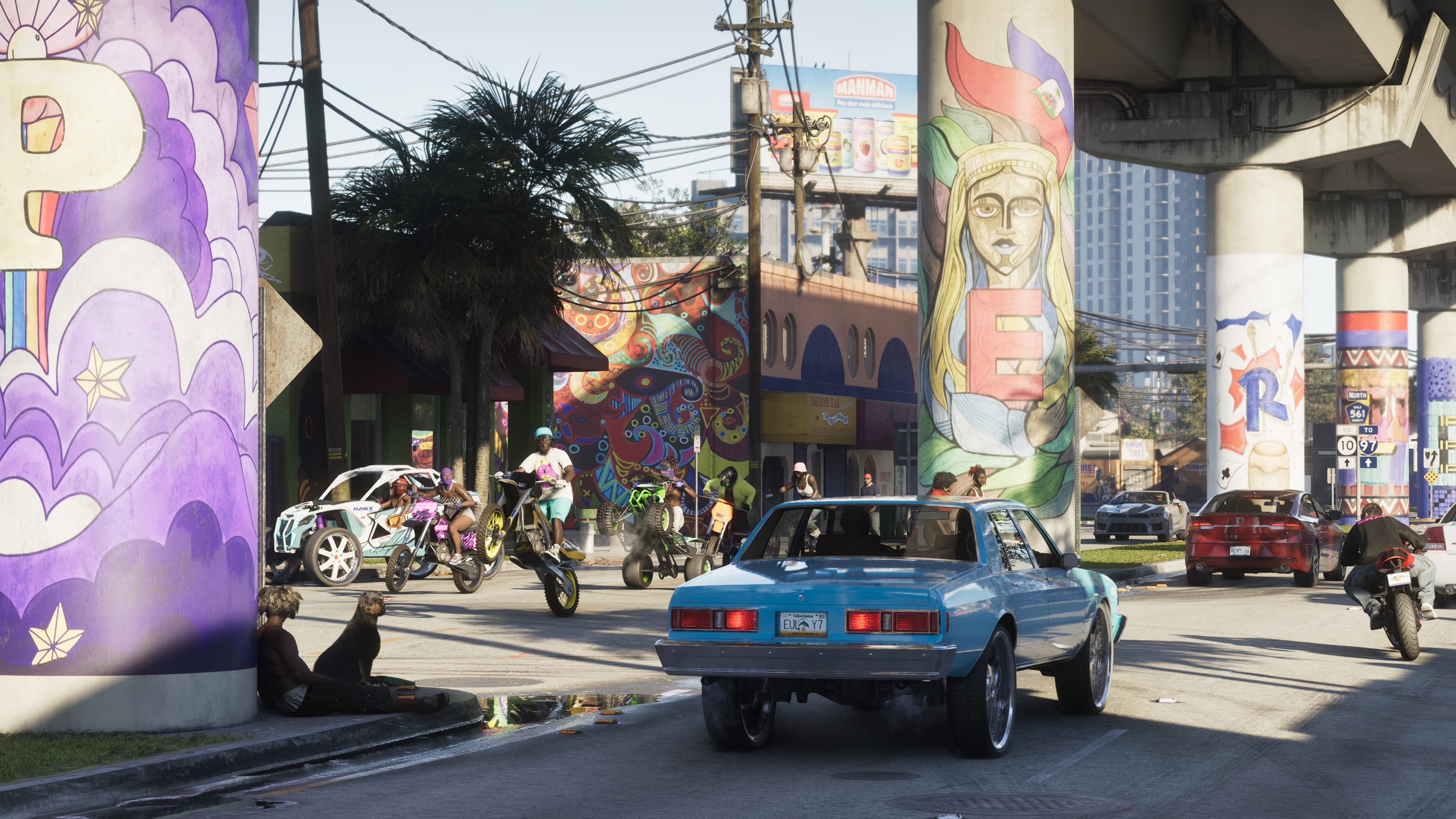 A street beneath a highway overpass with colourful murals on its pillars, a light-blue car, other traffic and motorcyclists.